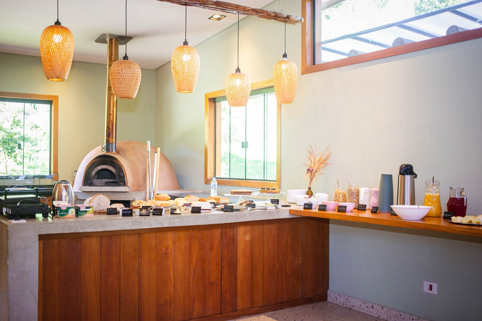 Mesa de buffet com forno a lenha, pães artesanais e bebidas naturais.